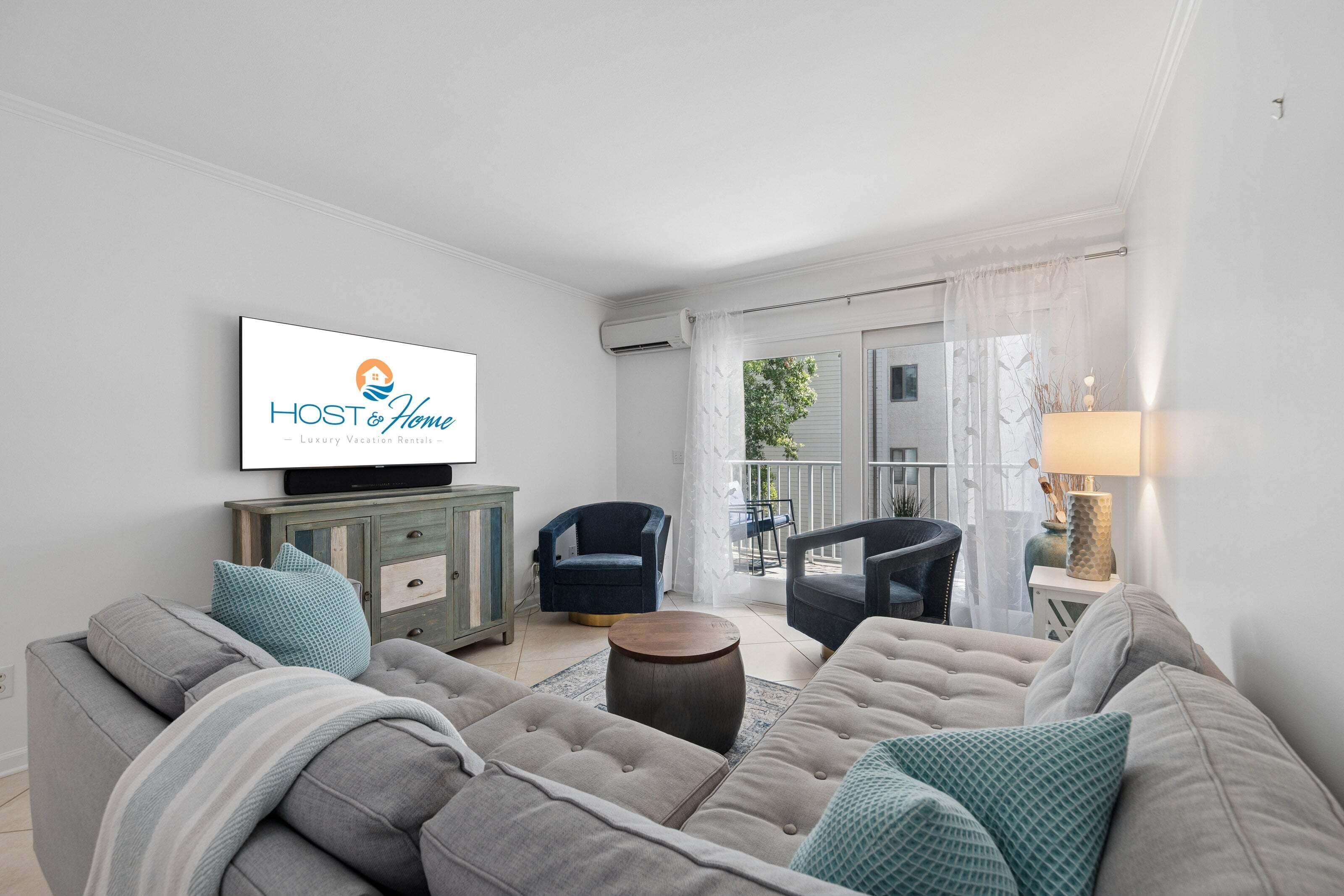 Ein Wohnzimmer mit einer Couch, Sesseln, einem Fernseher und Blick ins Freie.