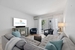 A living room with a sofa, armchairs, a television, and a view of the outdoors. - Forest Beach Condo | Community Pool | Oceanfront Private Beach Access | Elegant Furnishings (Hilton Head Island)