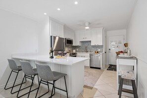 A modern kitchen with white cabinetry, a central island, bar stools, and a small dining table. - Forest Beach Condo | Community Pool | Oceanfront Private Beach Access | Elegant Furnishings (Hilton Head Island)
