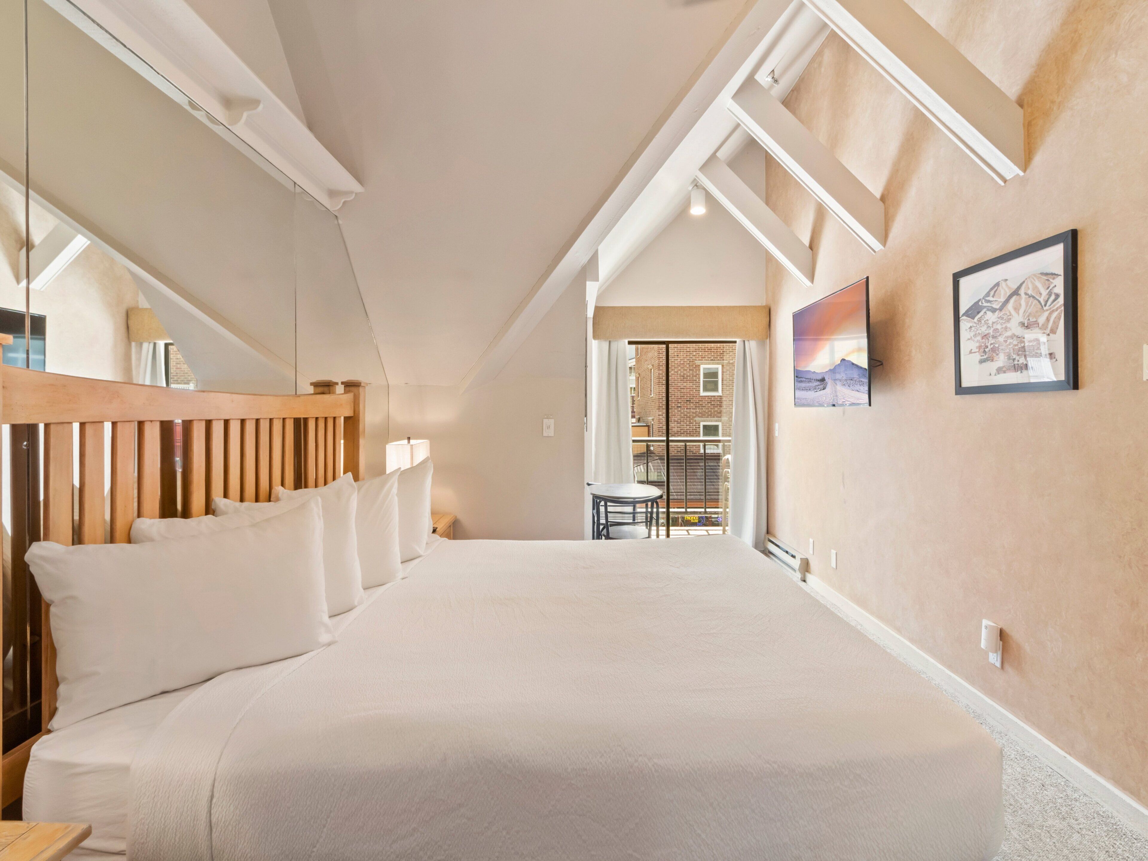 Una camera da letto con un letto grande, una testiera in legno, un comodino, una finestra e una porta che dà su un balcone.