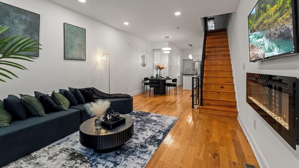 A modern living room with a dark sofa, a round coffee table, and a large flat-screen TV mounted on the wall. -   Modern 3BR Home Patio Near Center City Free Parkin (Philadelphia)