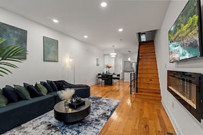 Ett modernt vardagsrum med en mörk soffa, ett runt soffbord och en stor, platt tv-skärm som är monterad på väggen.