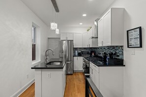 A modern kitchen with white cabinets, stainless steel appliances, a black countertop, and a kitchen island. -    Stylish Brewerytown Gem Near Center City Sleeps 8 (Philadelphia)