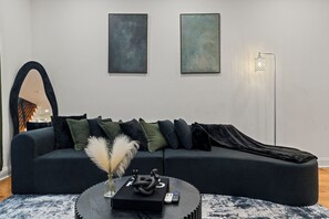 A modern living room with a dark-colored sofa, a round coffee table, and two abstract paintings on the wall. -    Stylish Brewerytown Gem Near Center City Sleeps 8 (Philadelphia)