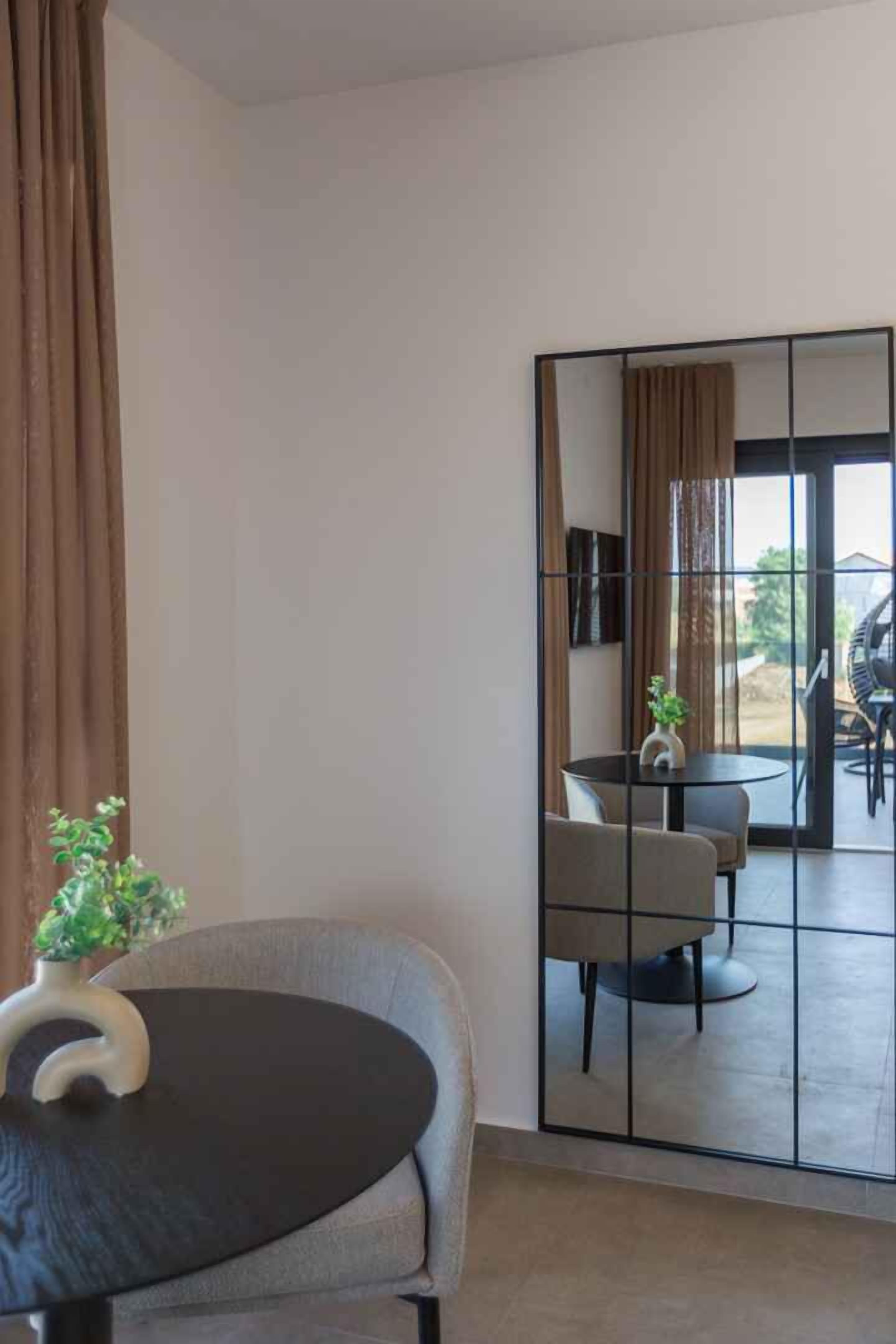 A modern room with a round table, a chair, a potted plant, a large mirror, and a sliding glass door leading to an outdoor area.