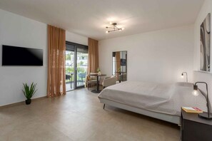A modern hotel room with a bed, a TV, a desk, and a balcony with a table and chairs. - Holiday Apartment Studio Apartment Valla (Funtana)