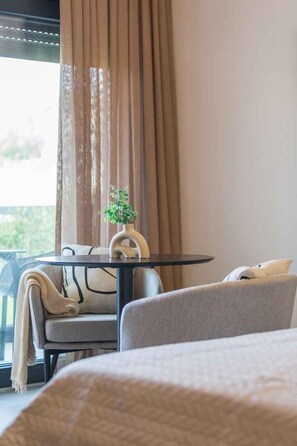 A hotel room with a bed, a small round table with a plant, a sofa, and a view through a window with curtains. - Holiday Apartment Studio Apartment Valla (Funtana)