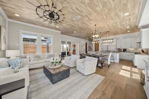 A spacious living room with a large sofa, a coffee table, and a dining area with a table and chairs. There is a kitchen area with cabinets and appliances. - Walk to Gulf Place~Private Pool~Dogs OK~EV Charger (Santa Rosa Beach)