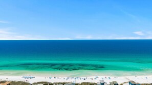 Ein Strand mit klarem türkisblauem Wasser, weißem Sand und einer Reihe von Strandsonnenschirmen.