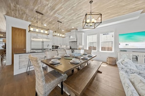 A modern kitchen with a central island, wooden flooring, and a dining area with a long table set for six. - Walk to Gulf Place~Private Pool~Dogs OK~EV Charger (Santa Rosa Beach)