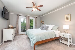 Una camera da letto con un letto, una ventola a soffitto, una TV, una cassettiera, un comodino con una lampada e una porta che dà su un balcone.