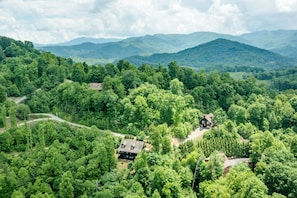 Un chalet isolé, entouré d’une forêt dense, accessible par un chemin sinueux.