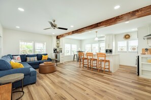 A spacious living area with a blue sofa, wooden dining table, and a kitchen with white cabinets and a wooden ceiling beam. - Fully Remodeled 2026– Beach Views, Steps to Beach (Freeport)