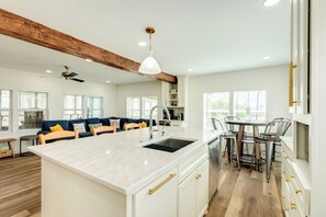 A modern kitchen with a central island, white cabinetry, and a dining area with metal chairs. - Fully Remodeled 2026– Beach Views, Steps to Beach (Freeport)