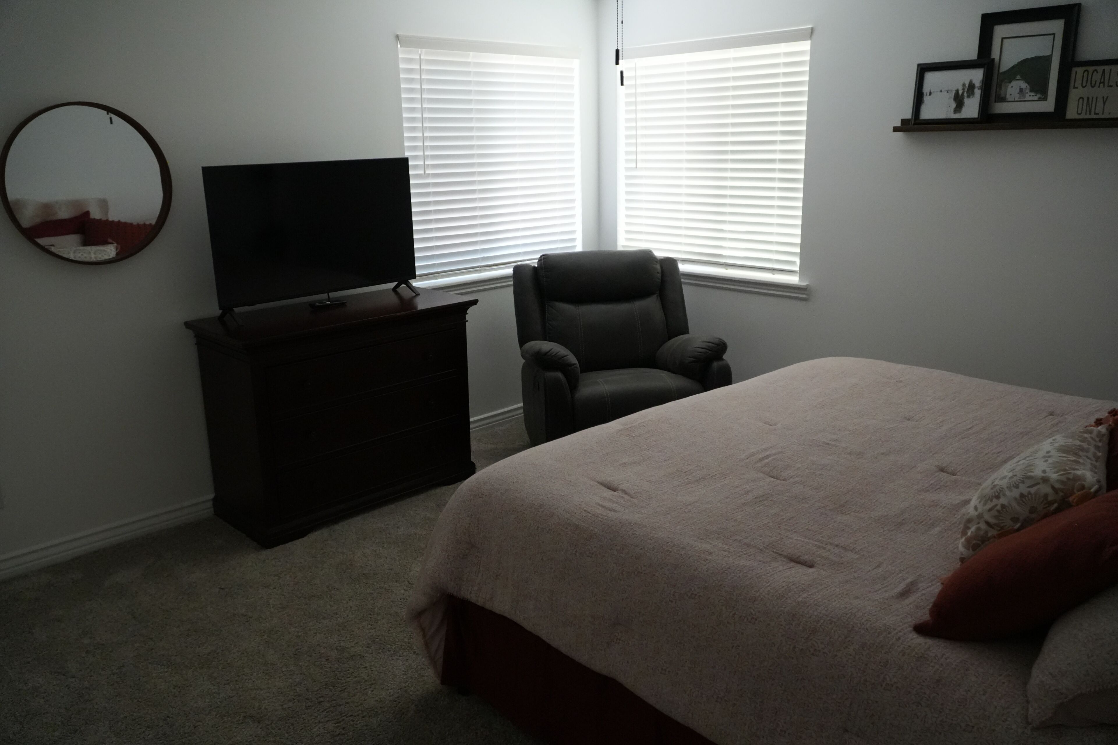 A bedroom with a bed, a chair, a TV on a dresser, and a window with blinds.