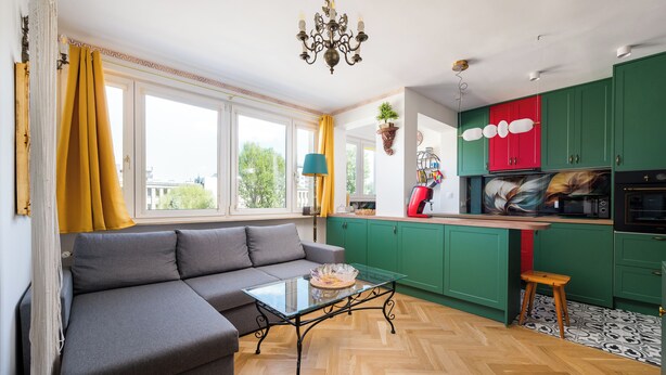 Een moderne keuken met groene kastjes, een grijze bank en een glazen salontafel.