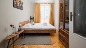 Quarto com cama de madeira, mesa de cabeceira com vaso e abajur, janela com cortinas e guarda-roupa.