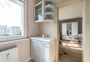 Een moderne keuken met witte kastjes, een raam met uitzicht op gebouwen en een eethoek met transparante stoelen.