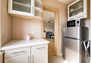 Una cocina compacta con muebles blancos, un refrigerador de acero inoxidable y un microondas.