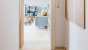 En hall som leder till ett vardagsrum med en soffa, en fåtölj och en telefon som är monterad på väggen.