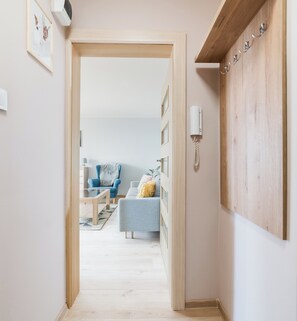 Un pasillo que da a una sala de estar con sofá, sillón y teléfono fijo en la pared.