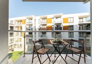 Ein Balkon mit zwei Holzstühlen und einem Tisch, mit Blick auf ein modernes Wohngebäude mit Balkonen.