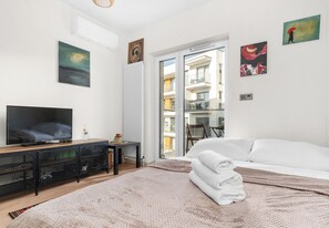 Ein Hotelzimmer mit Bett, Fernseher, Heizkörper, Fenster und Bildern an den Wänden.