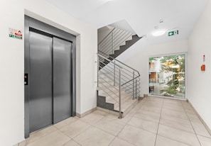 Un intérieur moderne avec un ascenseur métallique, un escalier doté de rampes en métal et une porte en verre donnant sur un espace extérieur.