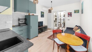 Uma cozinha moderna com armários verde-água, uma mesa de jantar com cadeiras e um sofá numa sala de estar.