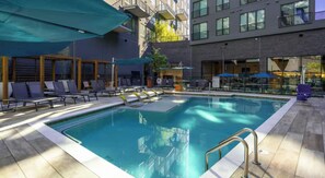 Una piscina con lettini e ombrelloni, circondata da un edificio con balconi e finestre.