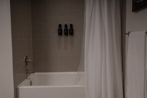 Un bagno con una vasca, un tendino doccia e tre flaconi di shampoo a parete.