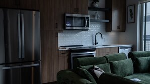 Moderni keittiö, jossa on ruostumattomasta teräksestä valmistetut kodinkoneet, sisäänrakennettu mikroaaltouuni ja vihreäverhoiltu sohva.