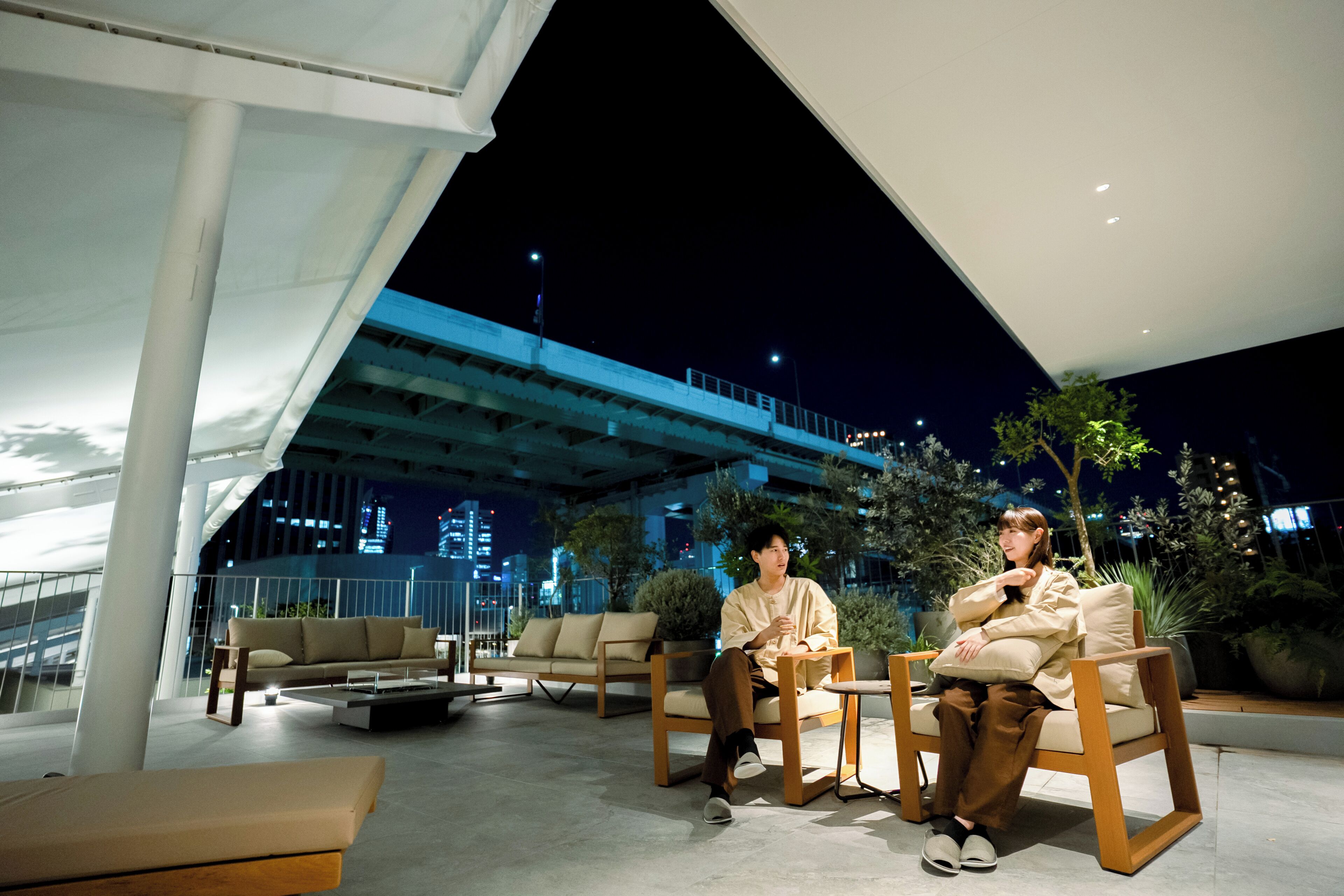 An outdoor seating area with modern furniture, a view of the cityscape, and a bridge in the background.