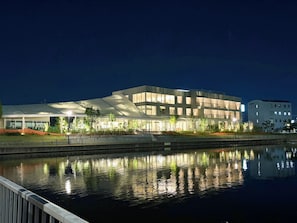 A modern building with a reflective water body in front, large windows, and a flat roof.