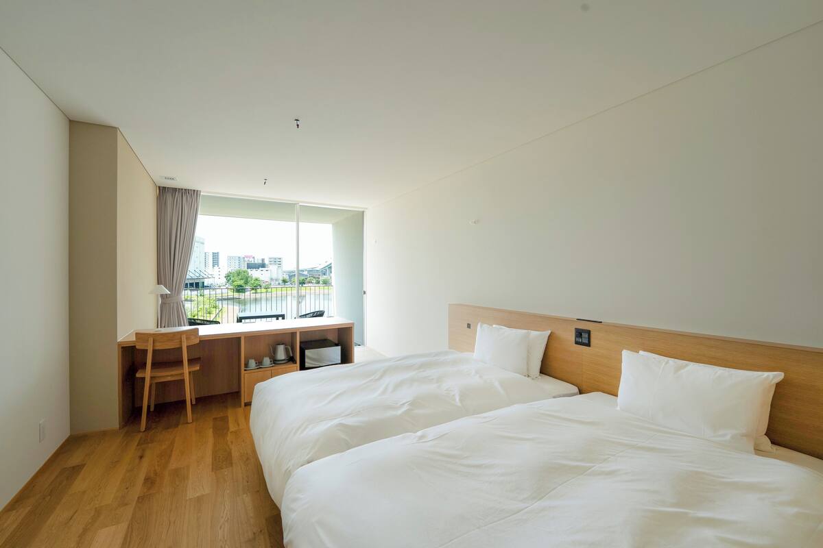 Une chambre d’hôtel avec deux lits, un bureau et une fenêtre donnant sur des immeubles.