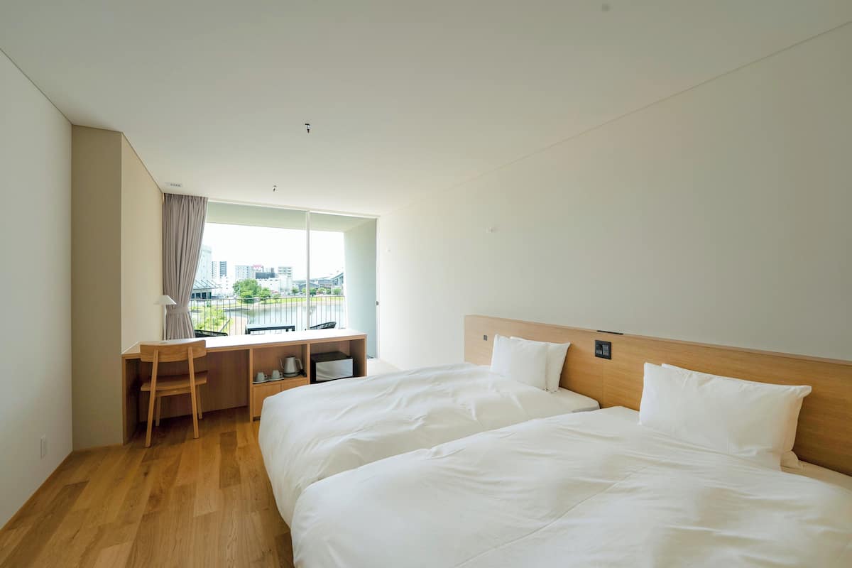 Une chambre dâhĂŽtel avec deux lits, un bureau et une fenĂȘtre donnant sur des immeubles.
