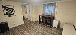 A compact kitchen with a wooden table, two stools, a refrigerator, and a wall-mounted sink. - Ideal Location! Peaceful and Comfy 1 bed/1 bath (Clarksville)