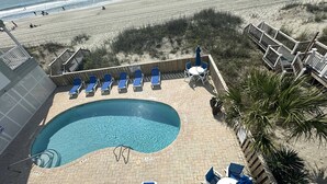 Een zwembadgedeelte met blauwe ligbedden, een klein zwembad en een houten terras met uitzicht op het strand.