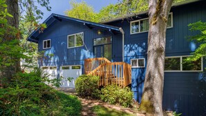 Une maison à deux étages, avec une façade bleue, un escalier en bois et un jardin agrémenté de différentes plantes.