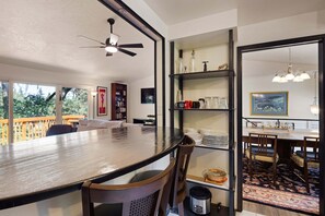 A dining area with a large table, chairs, a ceiling fan, and a view of the outdoors.