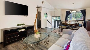 Un salon moderne avec un téléviseur à écran plat, une table basse en verre, un meuble de rangement en bois foncé et un canapé.