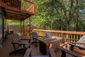 A wooden deck with Adirondack chairs, a fire pit, and a pergola.