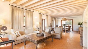 Un vaste espace de vie doté d’un plafond en bois, d’une grande table basse et d’un coin repas avec des meubles en osier.