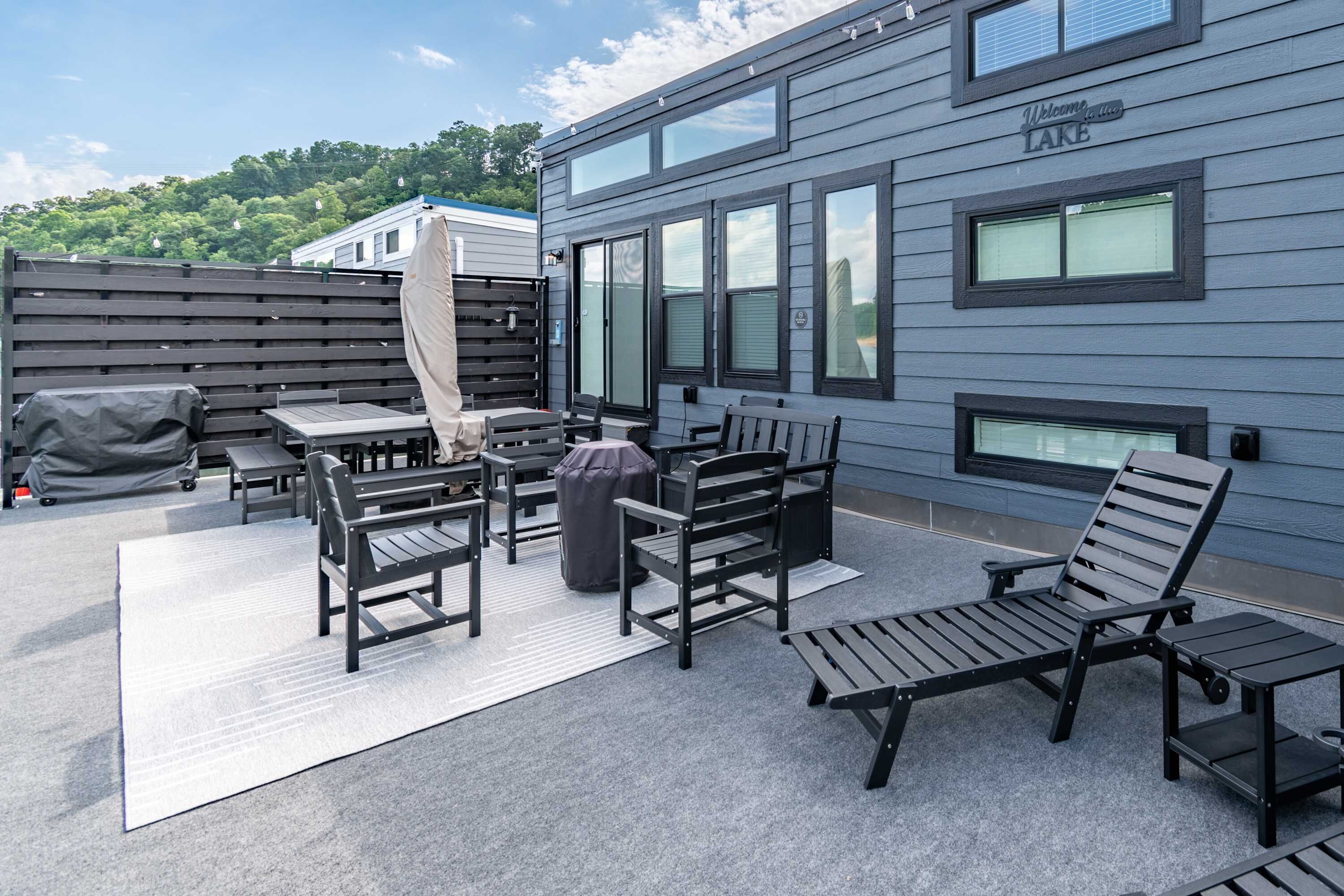 Un patio con mobiliario exterior, una parrilla cubierta y un edificio con un cartel de 'Welcome to Lake'.