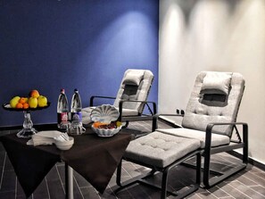 Ein Zimmer mit zwei Liegesesseln, einem Tisch mit Obstschale, Flaschen und einer Taschentuchbox.