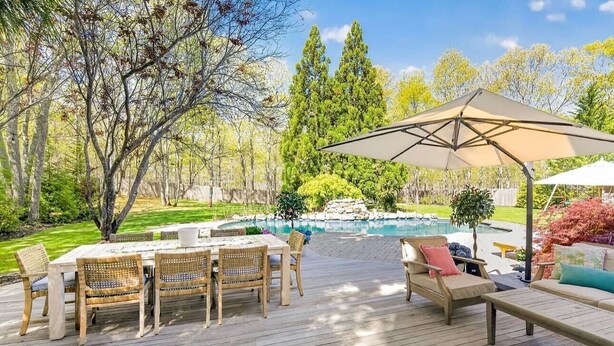 Une terrasse en bois avec une table et des chaises, un coin salon avec un canapé et un parasol, et une piscine en arrière-plan.