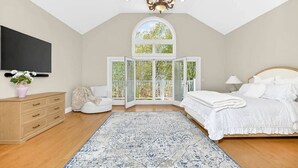 Une chambre à coucher avec un grand lit, une télévision, un lustre, une fenêtre et une commode en bois.