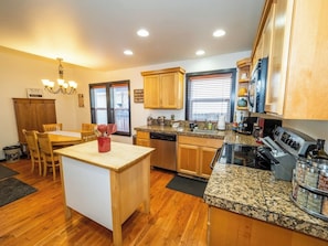 A kitchen with wooden cabinets, granite countertops, a dishwasher, a stove, and a dining area with chairs and a table.