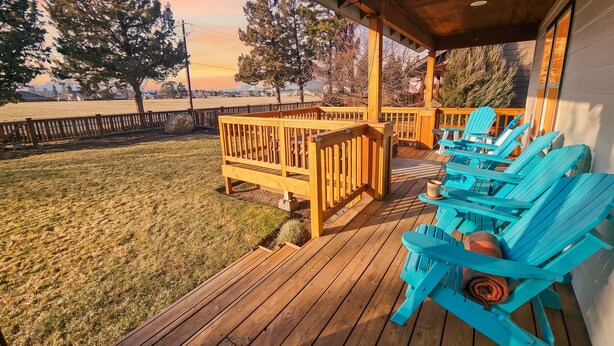 Eine Holzterrasse mit überdachtem Bereich, Sitzgelegenheiten im Freien und Blick auf Bäume sowie eine entfernte Landschaft.