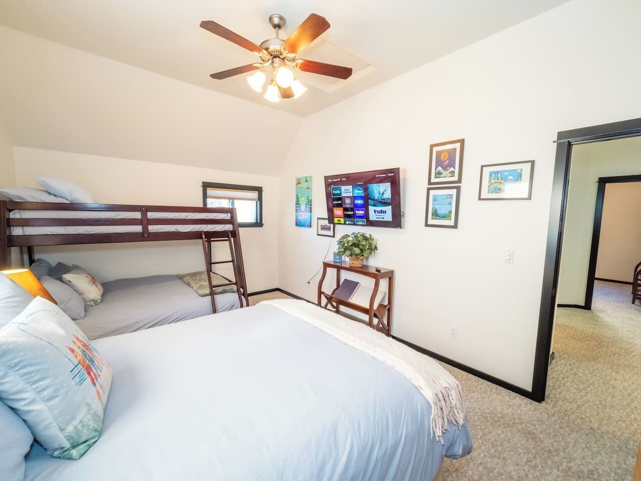 A bedroom with a bunk bed, a single bed, a ceiling fan, a TV, and a small table with a plant.